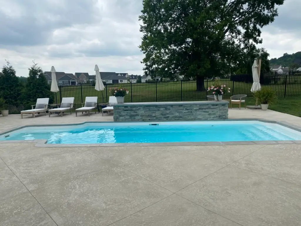 Stone-deck pool with waterfall and umbrella